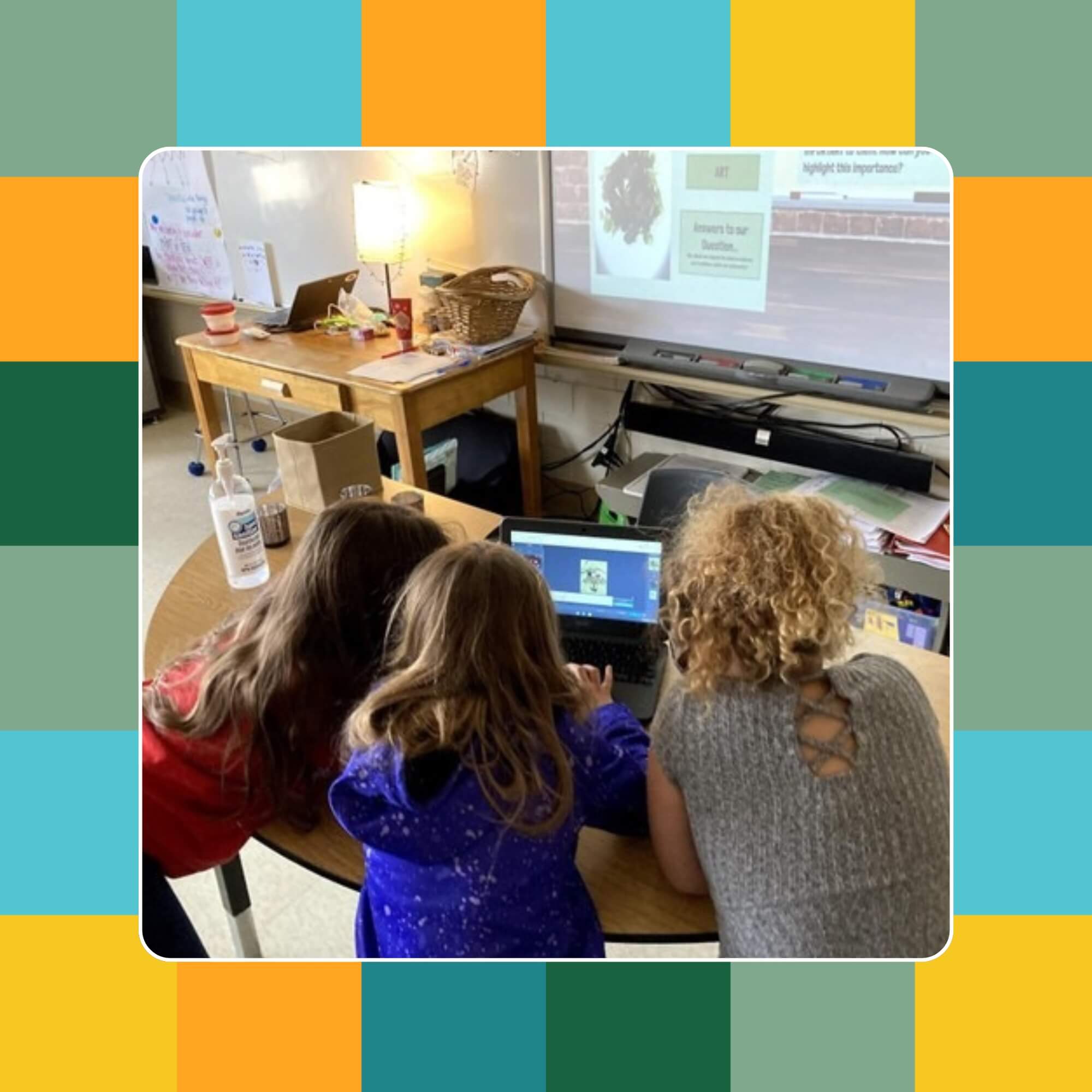 Three people gathered around a laptop in a classroom setting.