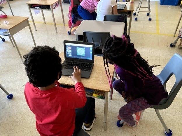 Two children working on a computer in a classroom setting.